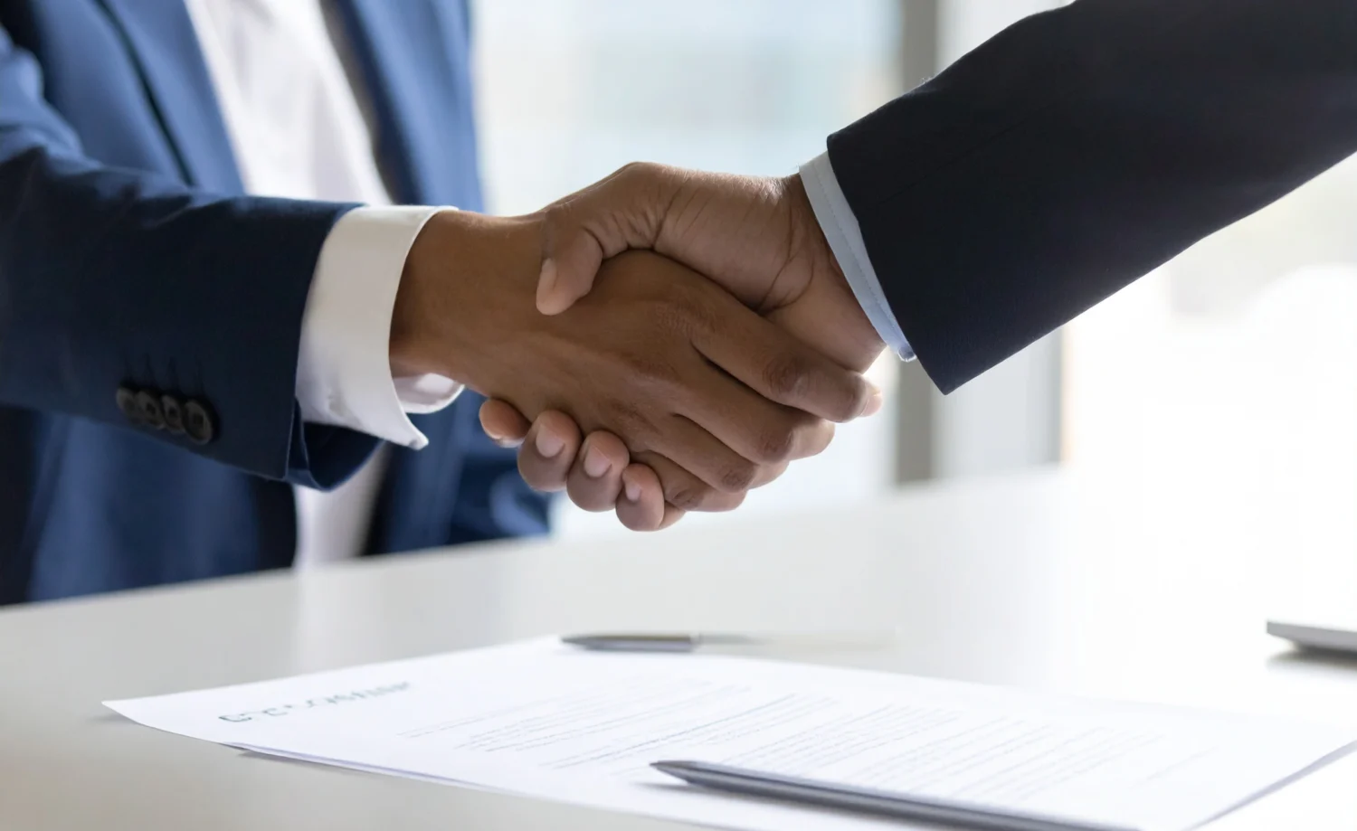Zwei Männer im Anzug geben sich einen Handschlag. Auf dem weißen Tisch liegt die Änderungskündigung und ein Stift.