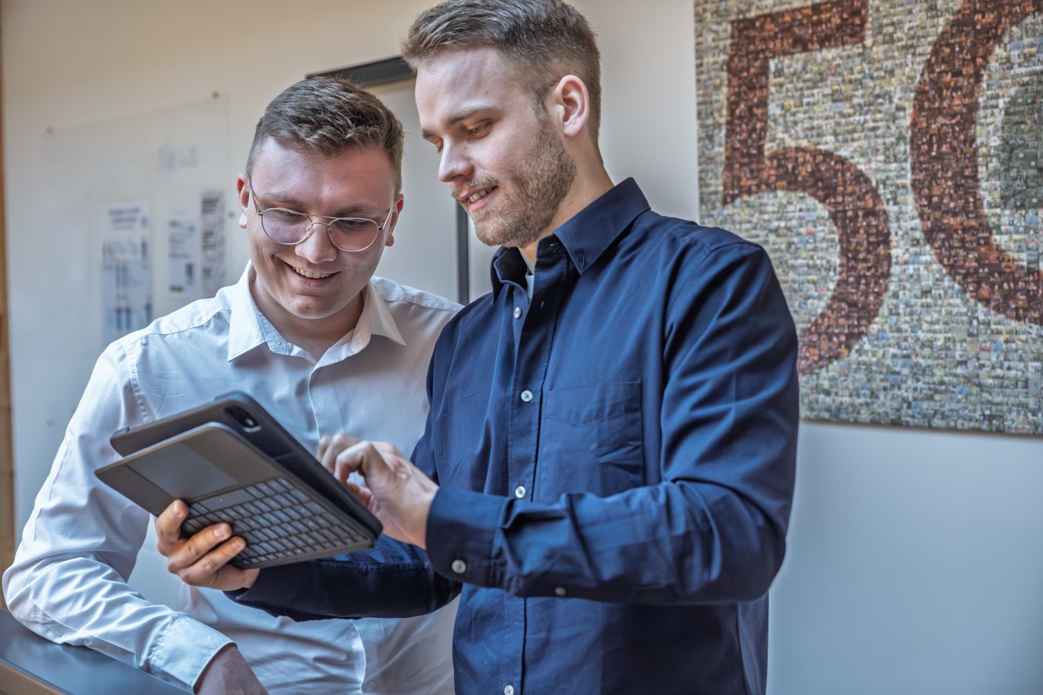 Foto von zwei jungen Männern die auf ein Tablet schauen.