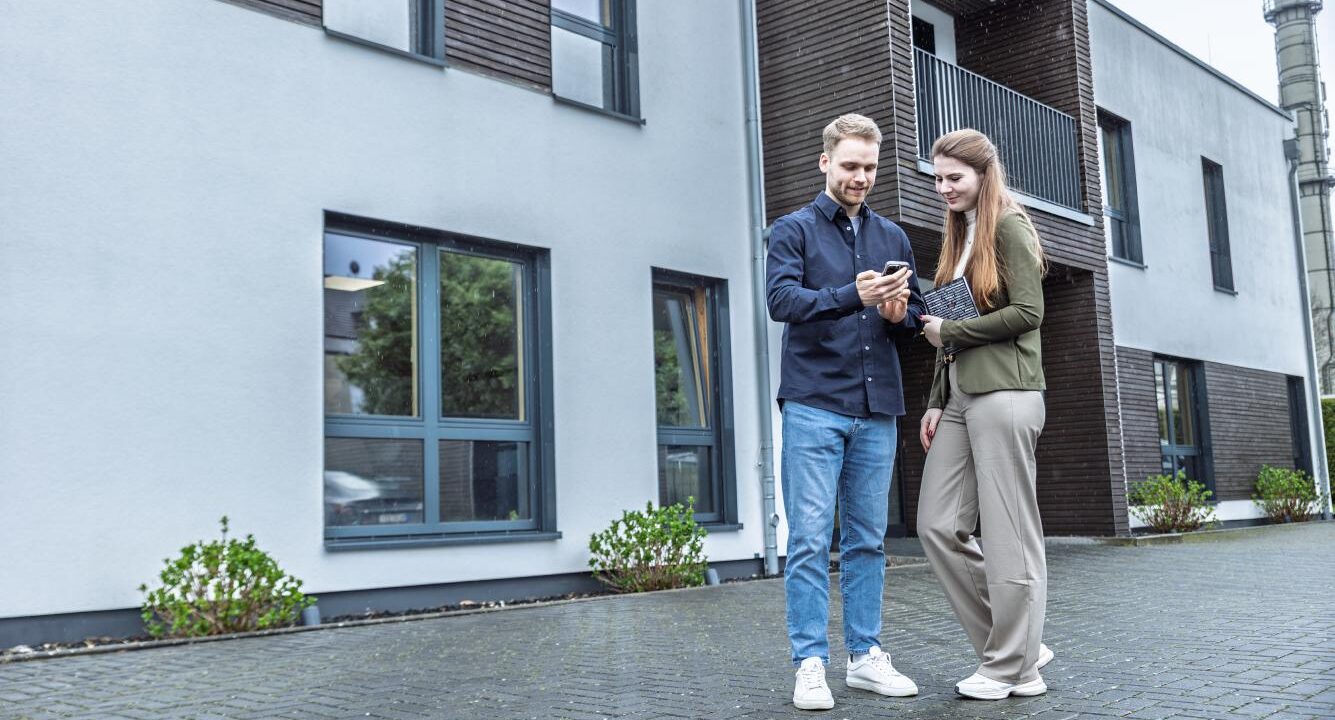 Zwei Mitarbeiter sind schauen vor einem Bürogebäude auf ein Handy.