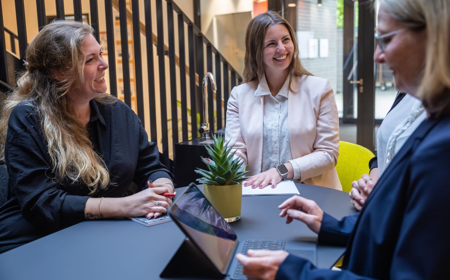 Das Foto zeigt drei Business-Frauen, die sich an einem Tisch unterhalten.
