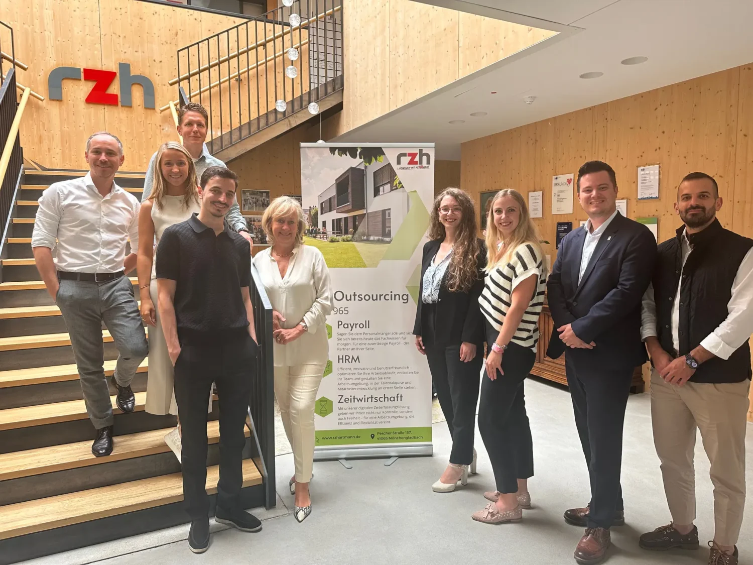 Insgesamt neun Personen stehen vor oder auf einer Treppe und lächeln in die Kamera.