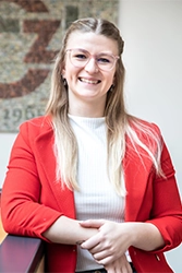 Bild einer jungen blonden Frau im weißen Oberteil und roten Blazer.