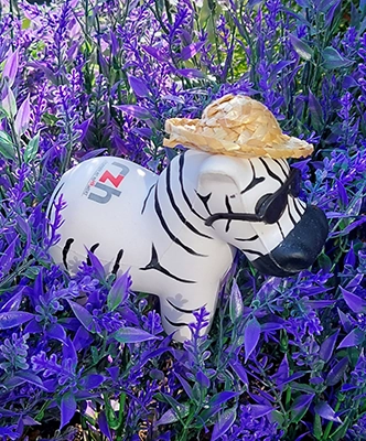 Darstellung des Maskottchen Hartmut mit Hut im lila Blütenmeer.